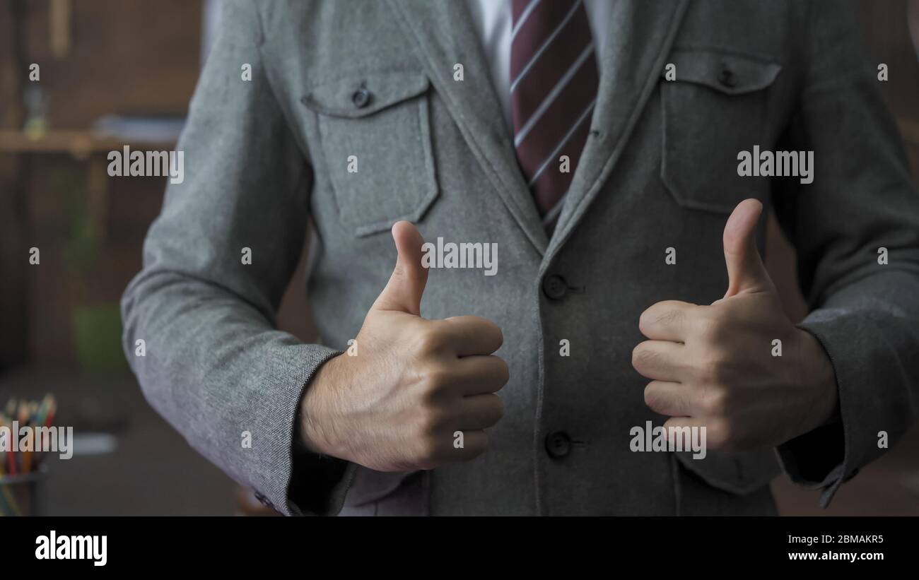 Successful businessman shows a thumbs up gesture. Male leader expresses positive emotions in order to cheer up his team. Successful business concept Stock Photo