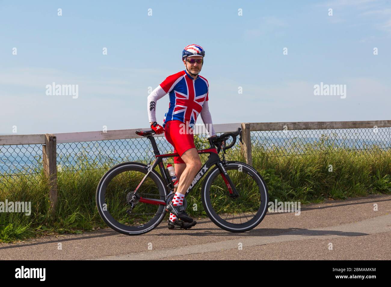 Bournemouth, Dorset UK. 8th May 2020. Nick shows his support  to celebrate VE day 75th Anniversary wearing red white and blue Union Jack clothing on his bike ride on a lovely warm sunny day, as organised events are cancelled due to Coronavirus restrictions. Cyclist bike bicycle. Credit: Carolyn Jenkins/Alamy Live News Stock Photo