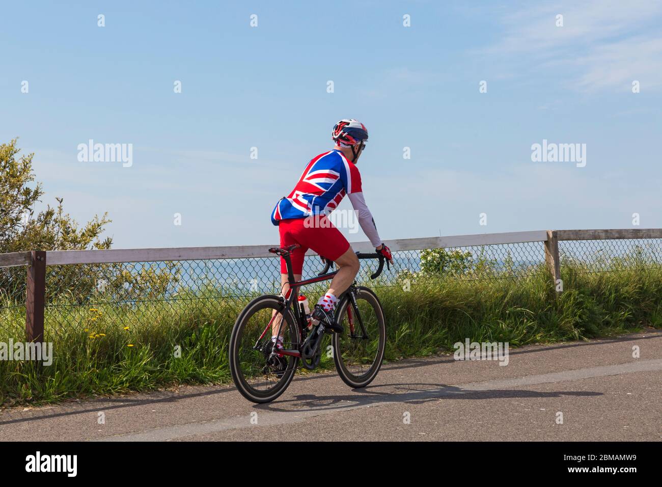Bournemouth, Dorset UK. 8th May 2020. Nick shows his support  to celebrate VE day 75th Anniversary wearing red white and blue Union Jack clothing on his bike ride on a lovely warm sunny day, as organised events are cancelled due to Coronavirus restrictions. Cyclist riding bike bicycle. Credit: Carolyn Jenkins/Alamy Live News Stock Photo