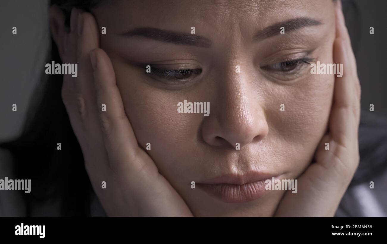 Close up of tired doctor fase sleepily rested on her hands. Sleepy Overworked Asian woman propped her head on hands looking at side. Unhappy Medic Stock Photo