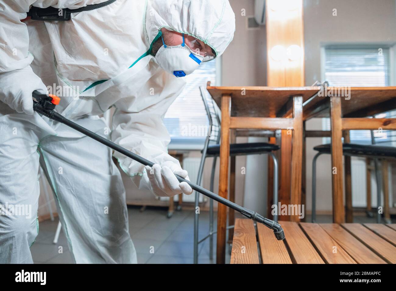 Coronavirus Pandemic. A disinfector in a protective suit and mask sprays disinfectants in house or office. Protection against COVID-19 disease. Prevention of spreding pneumonia virus with surfaces. Stock Photo