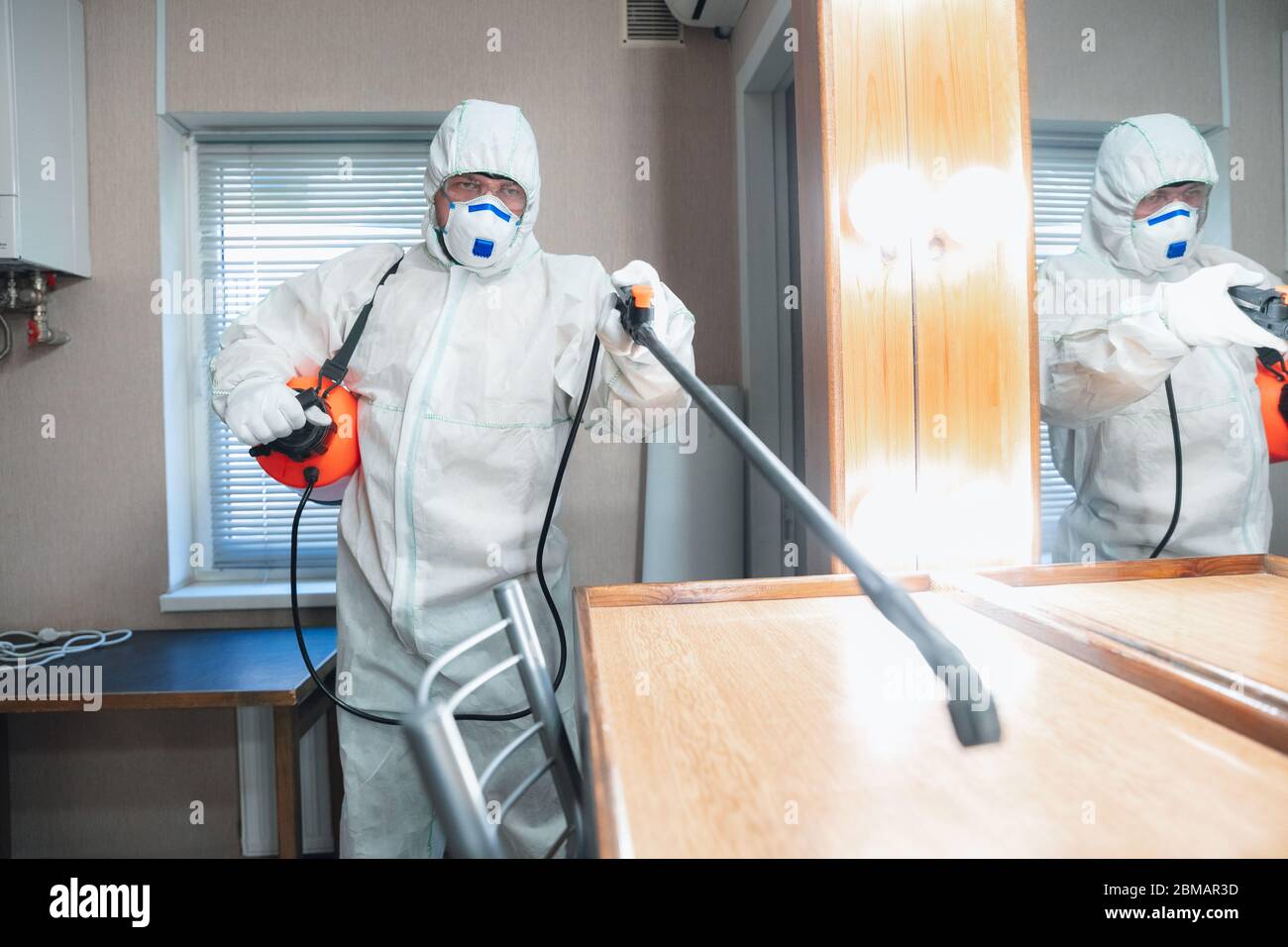 Coronavirus Pandemic. A disinfector in a protective suit and mask sprays disinfectants in house or office. Protection against COVID-19 disease. Prevention of spreding pneumonia virus with surfaces. Stock Photo