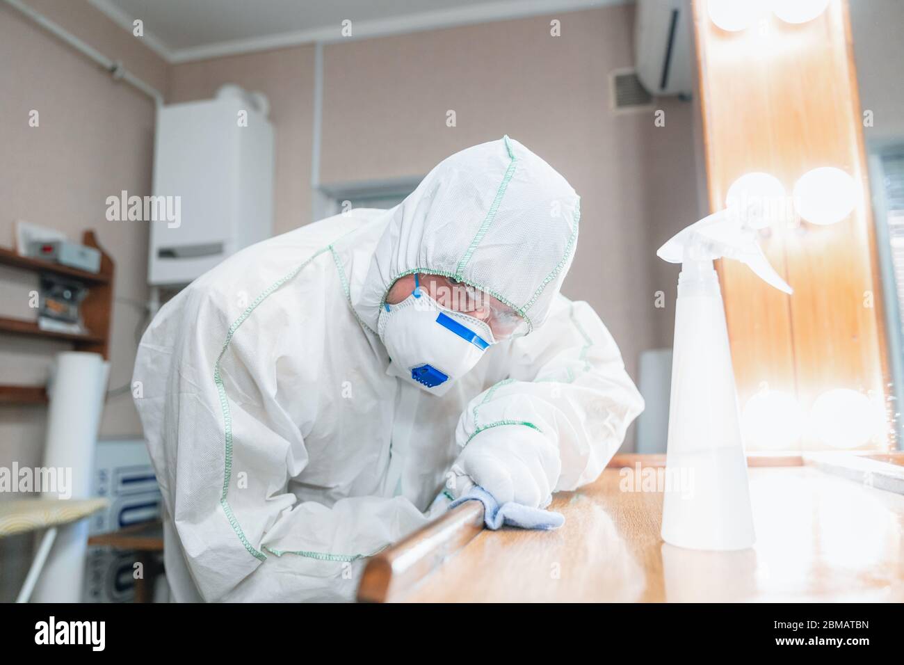 Coronavirus Pandemic. A disinfector in a protective suit and mask sprays disinfectants in house or office. Protection against COVID-19 disease. Prevention of spreding pneumonia virus with surfaces. Stock Photo