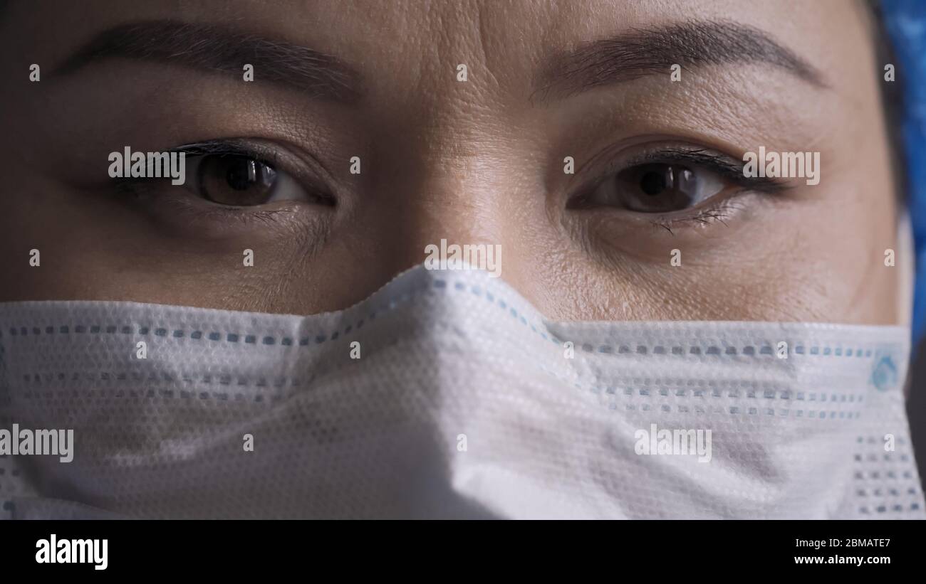Close up of tired doctor eyes. Woman wearing protective mask looking at camera. Medic feels stress after a long overtime Stock Photo