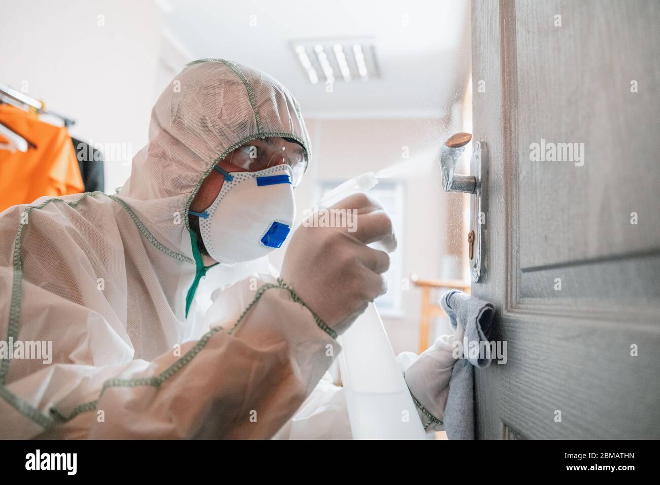 Coronavirus Pandemic. A disinfector in a protective suit and mask sprays disinfectants in house or office. Protection against COVID-19 disease. Prevention of spreding pneumonia virus with surfaces. Stock Photo