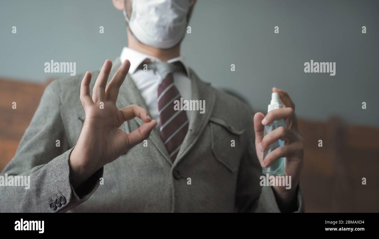 Businessman shows ok gesture holding a sanitizer or antiseptic liquid. Close up shot. Positive man in a protective mask works in the office during an Stock Photo