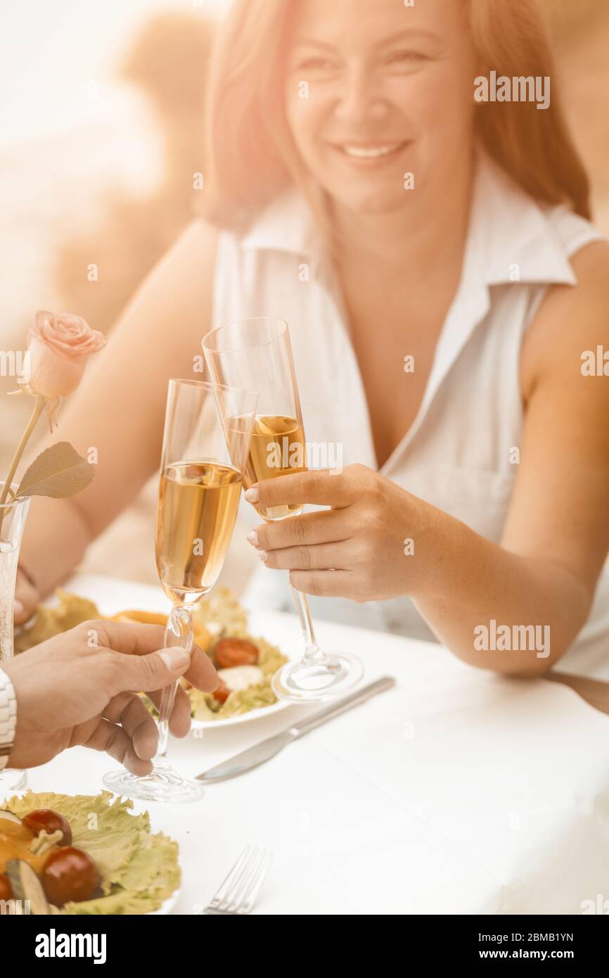 Happy woman smiles holding glass of white wine. Mature couple have event outdoors at beach cafe. Selective focus on human hands with glasses of wine Stock Photo