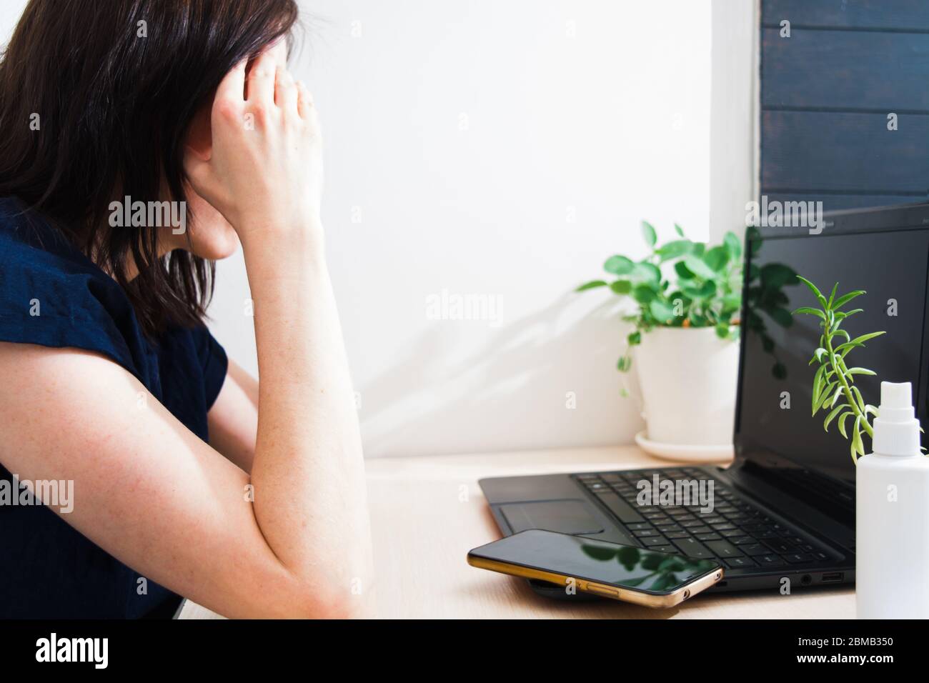 Sadness young woman with dark hair sitting at table, holding her head and looking on laptop. Remote work. Problem with online work. Online shopping co Stock Photo