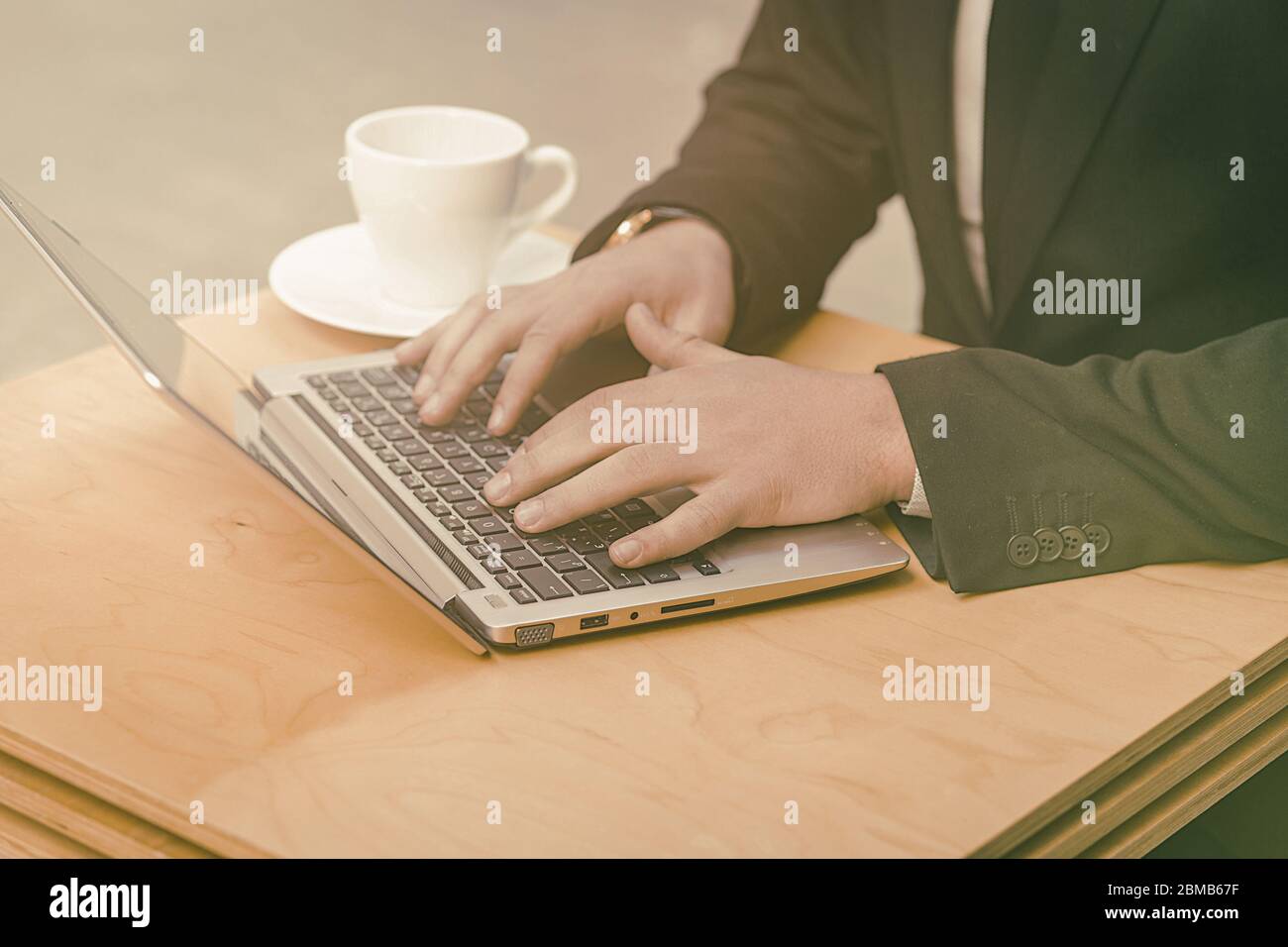 Businessman using laptop computer at street cafe outdoors. Close up shot of males hands typing at laptop keyboard. Business on the go concept. Toned Stock Photo