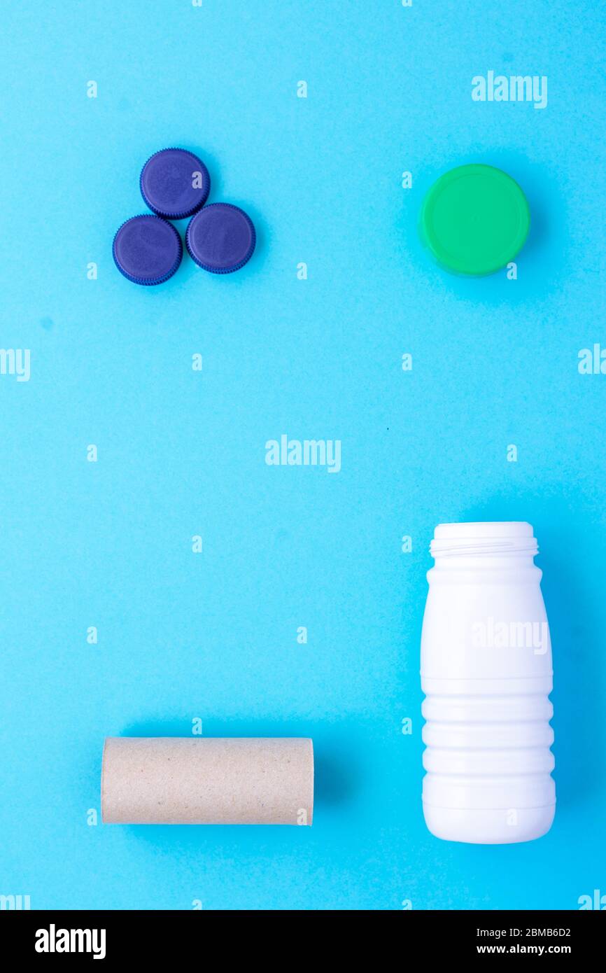 Recycling garbage. White plastic bottle, green cap, blue caps, finished paper roll arranged in a square shape on a blue background Stock Photo