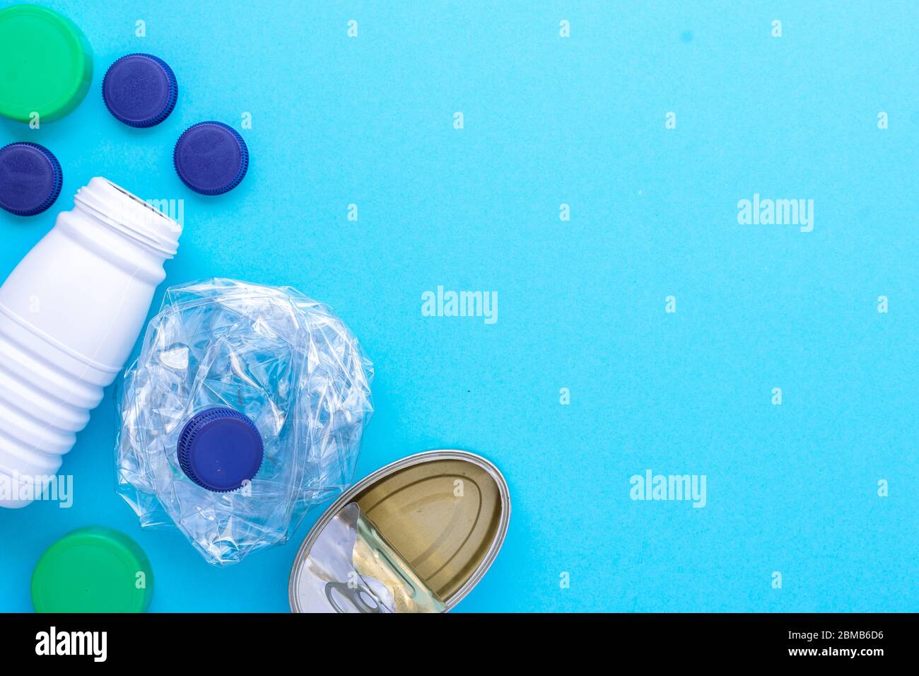 Recycling garbage. White plastic bottle, green cap, blue caps, can of sardines grouped on the left side diagonal on a blue background. Stock Photo