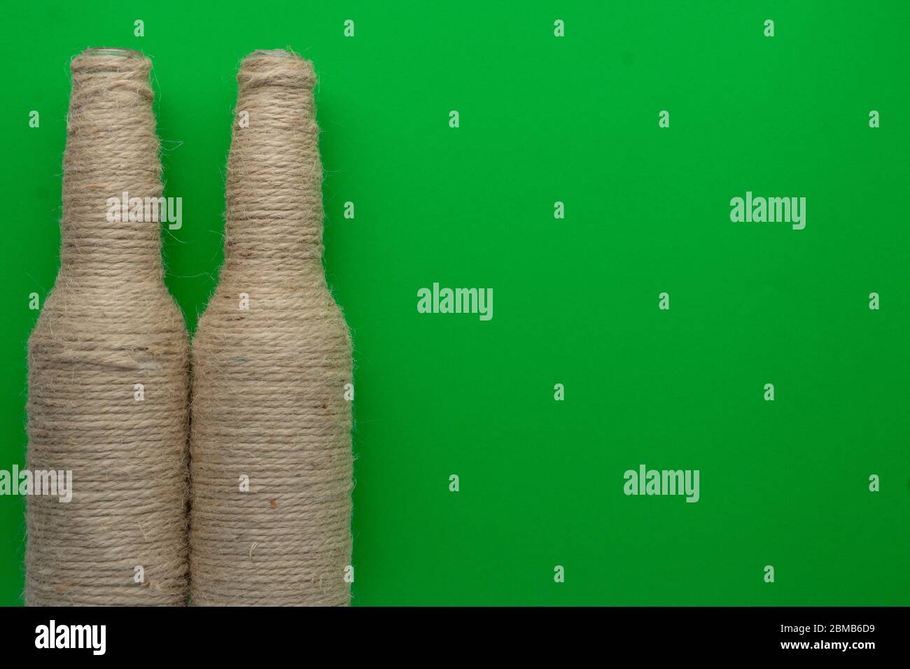 Two glass bottles of beer reused with hemp yarn on the left with a green background. Recycling and reusable concept Stock Photo