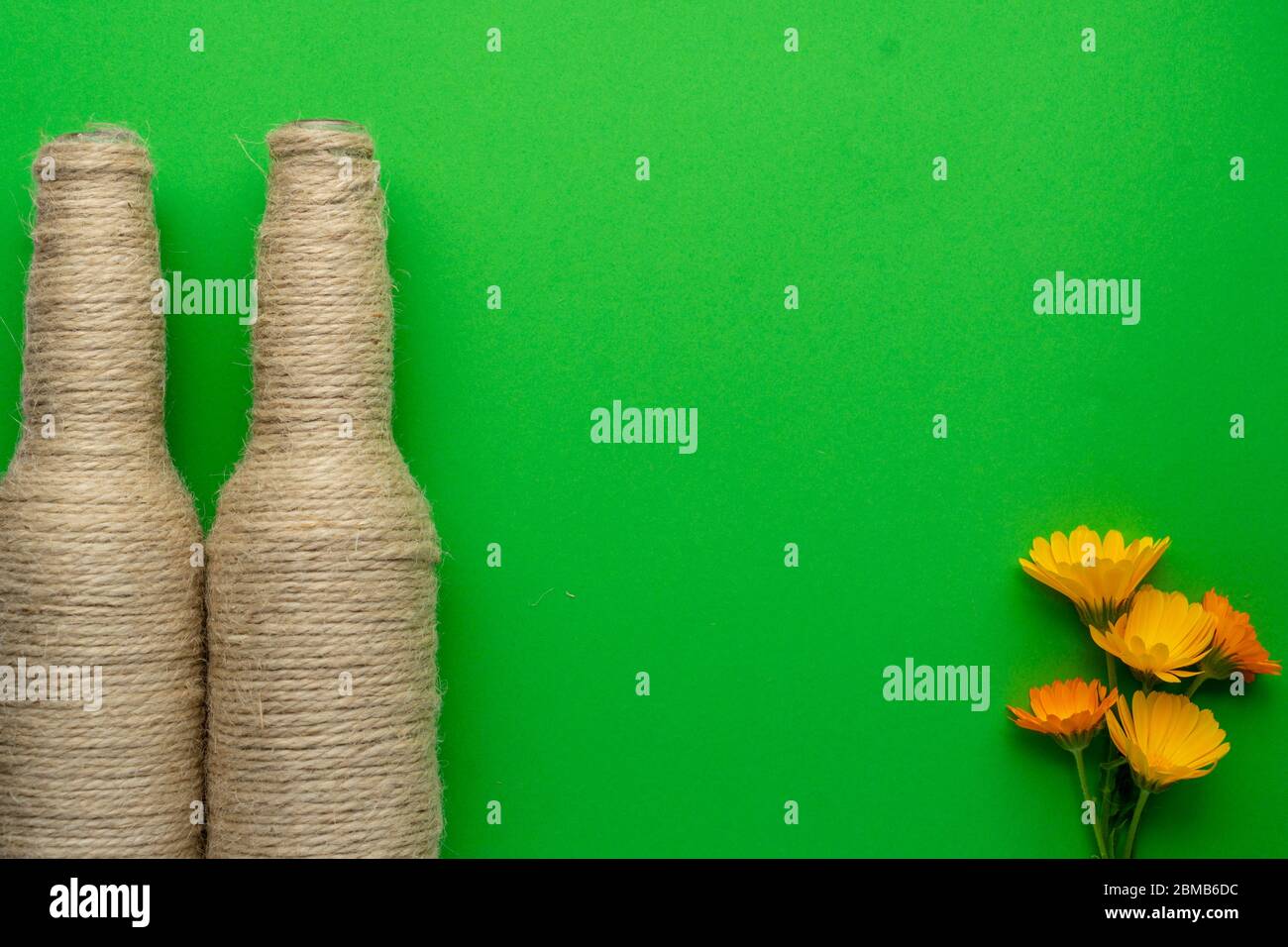 Two glass bottles of beer reused with hemp yarn and flowers on the left with a green background. Recycling and reusable concept Stock Photo