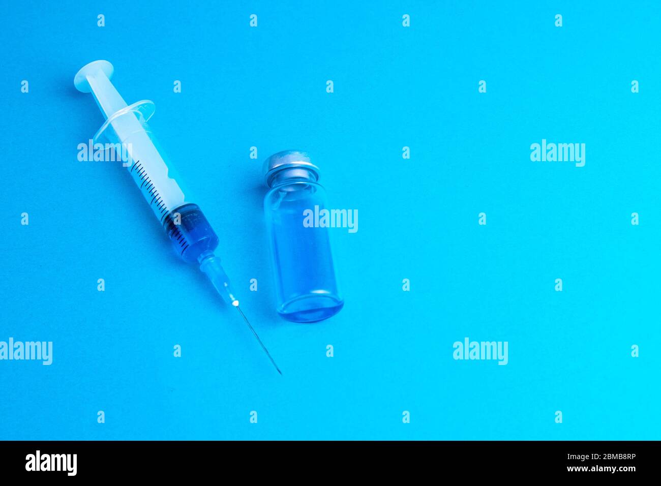 Glass vials and a medical syringe with a coronavirus vaccine on a blue ...