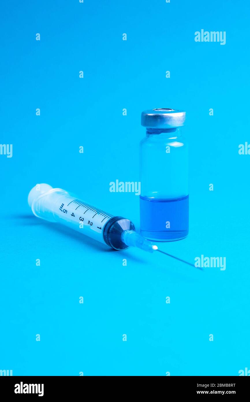 Glass vials and a medical syringe with a coronavirus vaccine on a blue ...