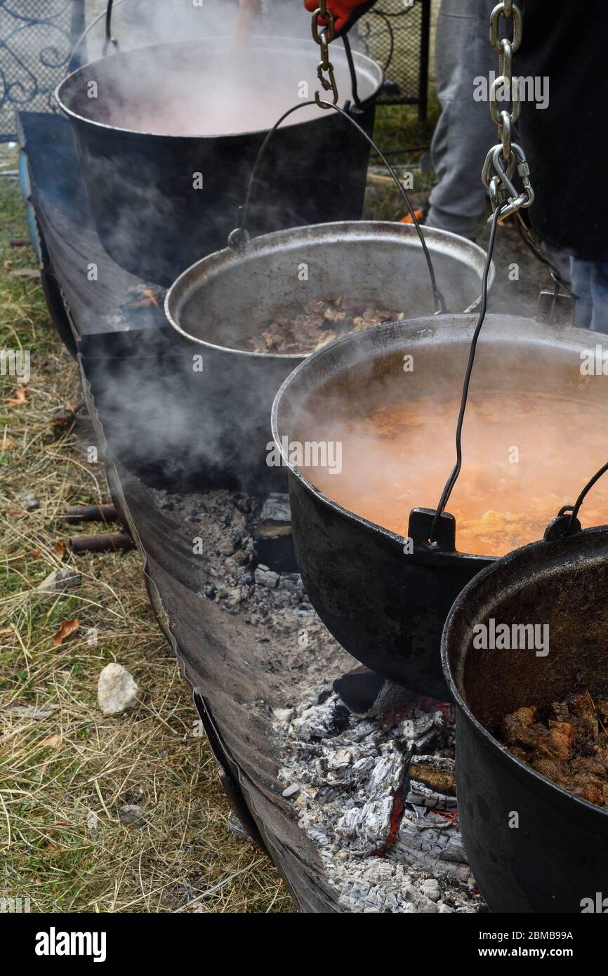 Very large cauldron cooking food during campfire, big pots on fire preparing during food festival. Tourist pot hanging over the fire on a tripod. Cook Stock Photo