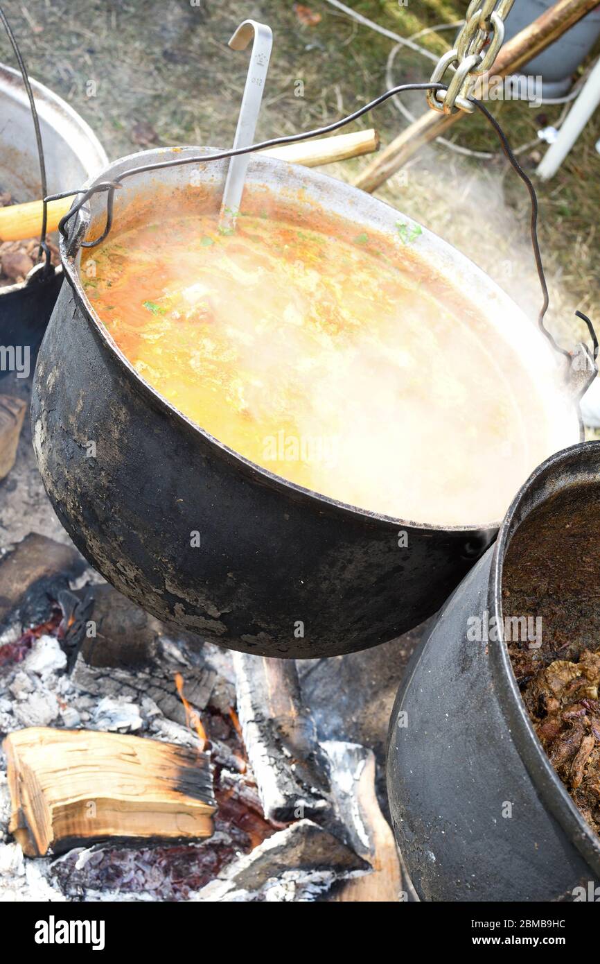 Very large cauldron cooking food during campfire, big pots on fire