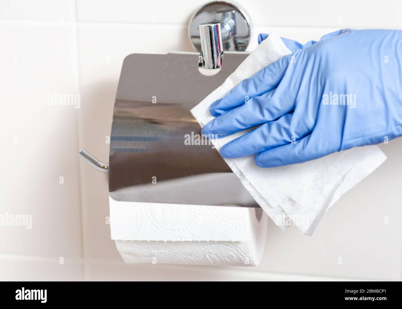 Maid with surgical gloves cleaning toilet paper holder with