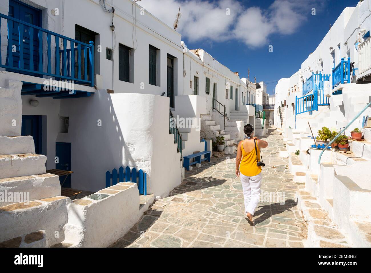 A woman walking down a street past traditional whitewash buildings in Folegandros, Cyclades Islands, Greece Stock Photo