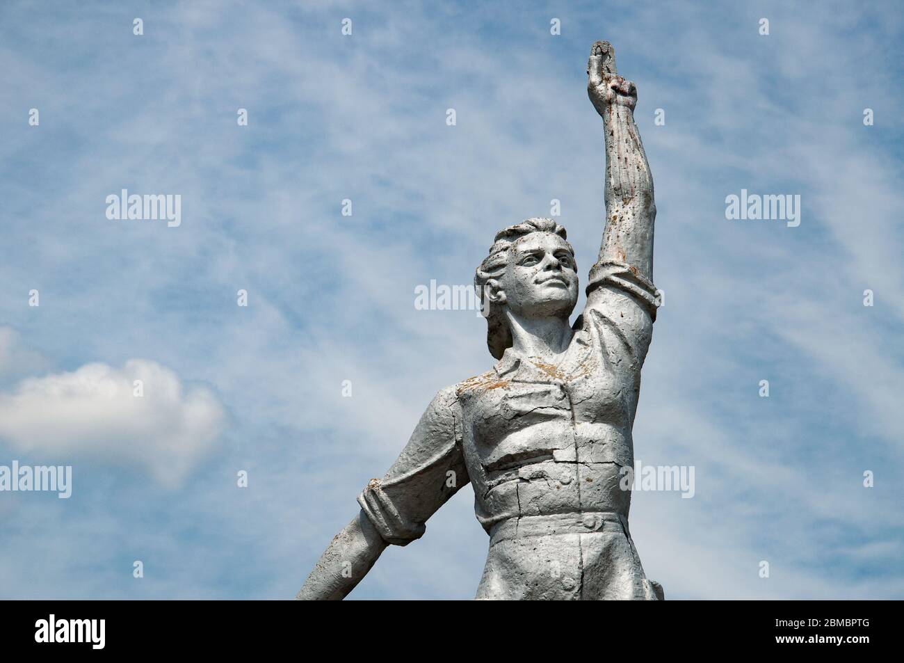 Closeup of old dilapidated stone statue of Soviet woman with rising hand on sky background Stock Photo