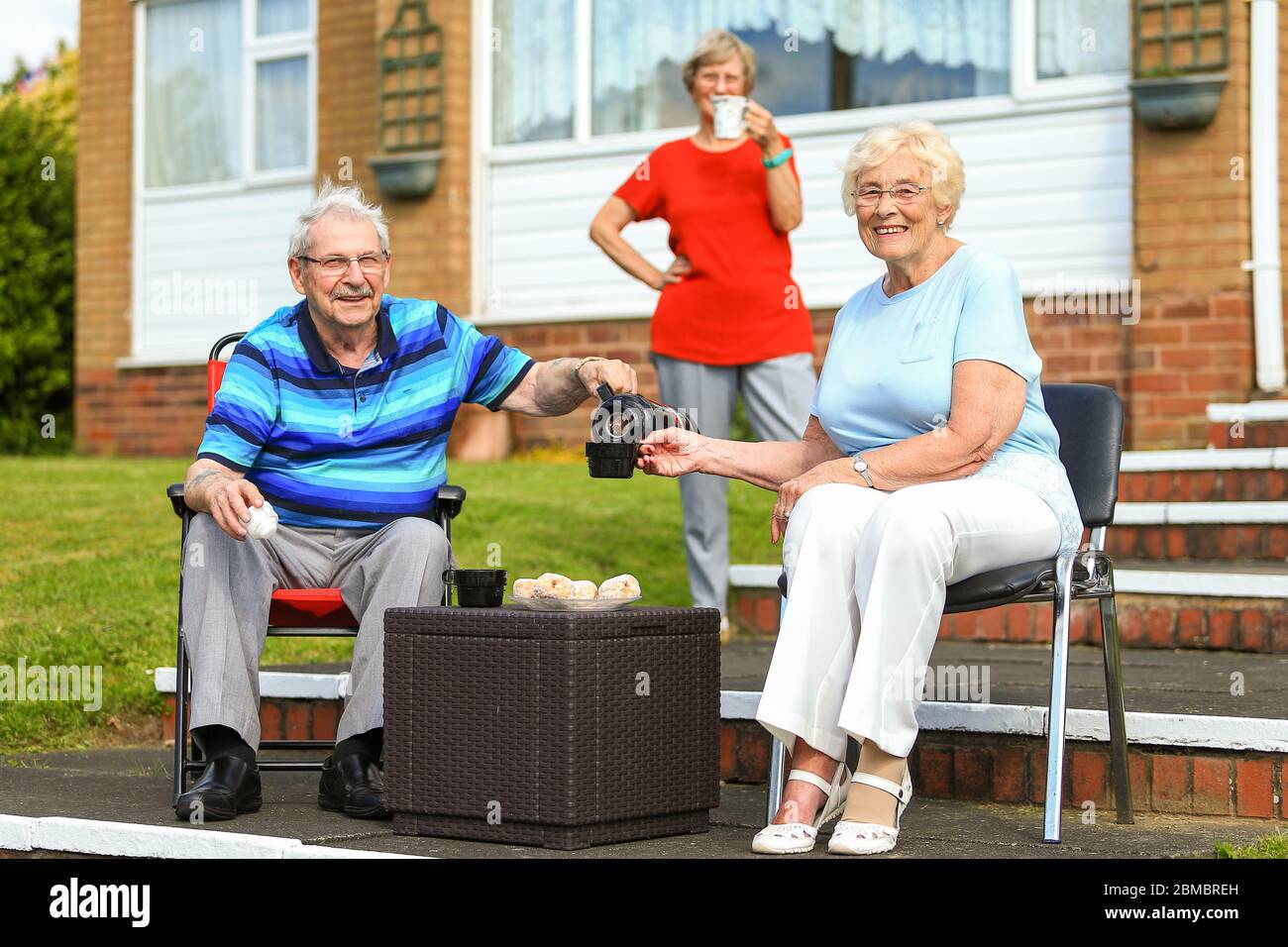 Halesowen, West Midlands, UK. 8th May, 2020. Husband and wife Jean and Michael Towler, 84 and 83, enjoy a very British flask of tea with neighbour Stella Worton outside their houses in Halesowen, West Midlands. Credit: Peter Lopeman/Alamy Live News Stock Photo