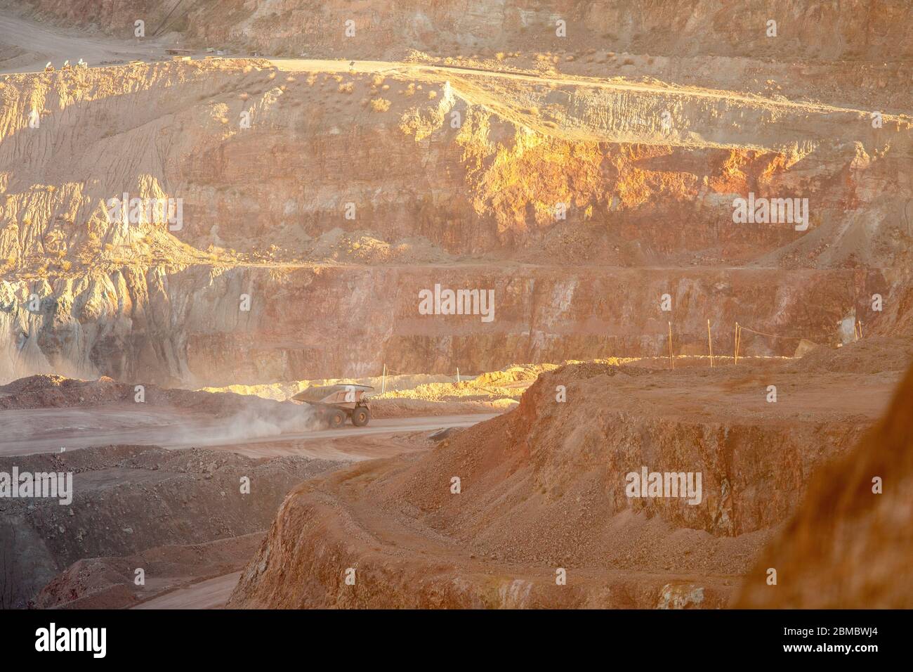 A dump truck kicks up dust at sunset as it hauls dirt in a strip mine ...