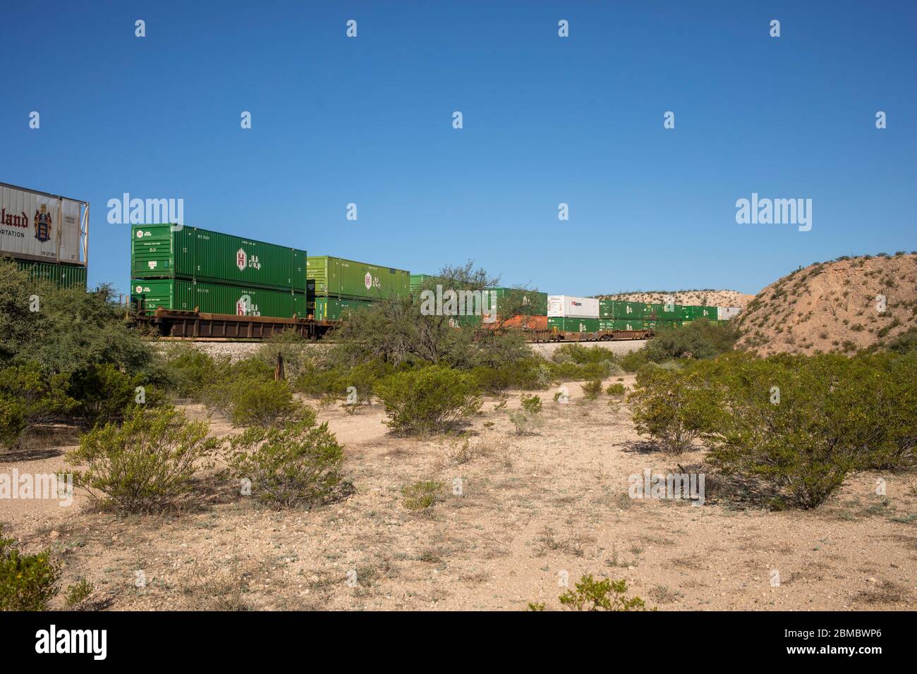 A train of container cars rolls through a desert landscape left frame Stock Photo