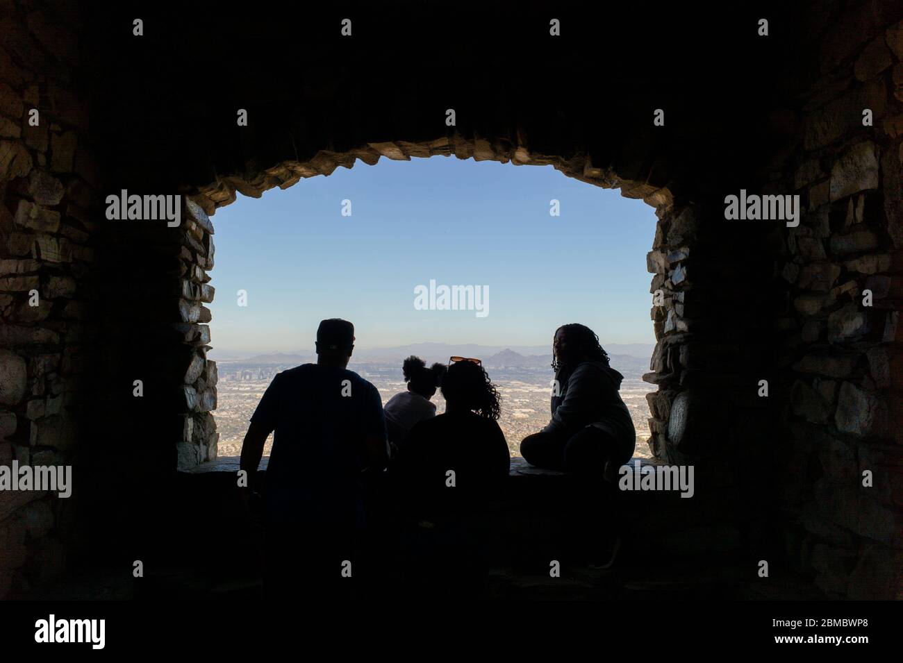 Family silhouetted looking out opening in rock wall over Phoenix Stock Photo