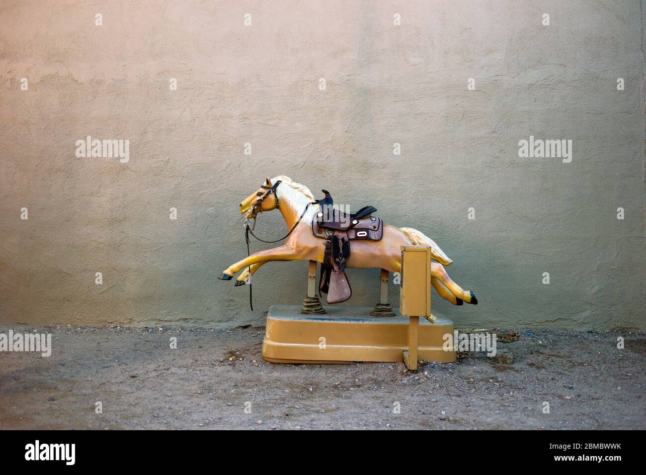 A toy riding horse coin operated machine against plain wall in dirt