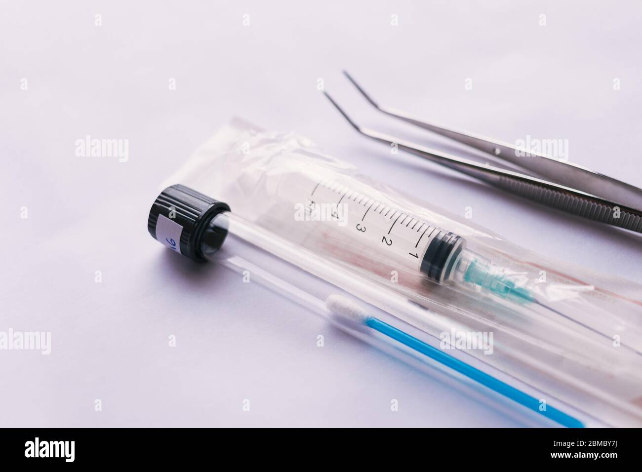 A syringe and a pair of tweezers with a test swab inside a test tube
