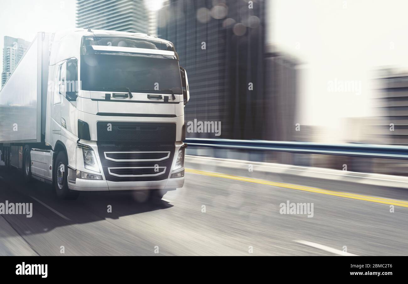 White truck moving fast on the highway with a modern city in the background Stock Photo