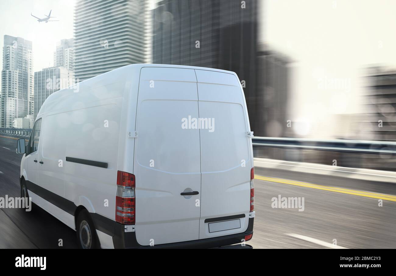 White van moving fast on the highway with a modern city in the background Stock Photo