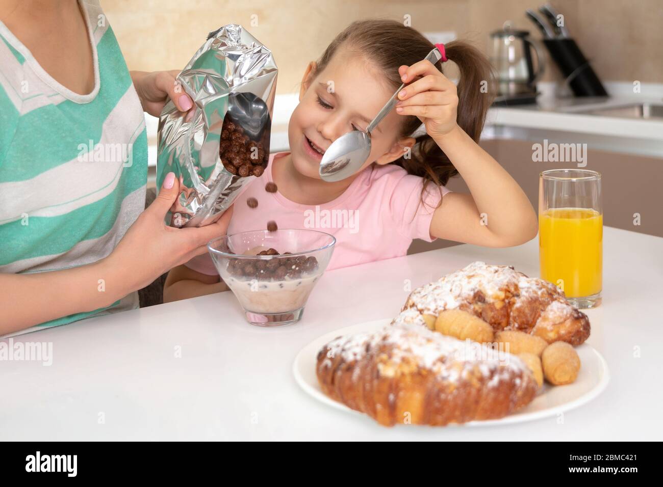 Mother having breakfast with her daughter at a table in kitchen, happy single mother concept Stock Photo