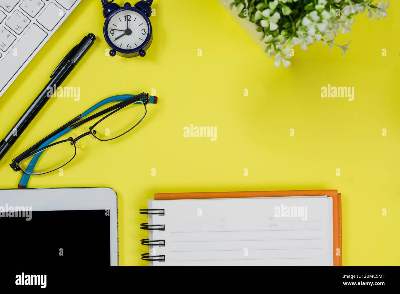 Bright yellow office desk table with notebook, keyboard, clock, pen and
