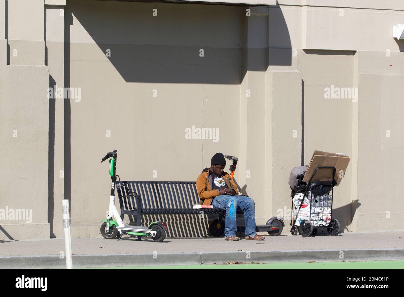 A homeless man naps on the street in the SoMa neighborhood of San Francisco, California. Frye Gaillard's book A HARD RAIN is seen on the bench. Stock Photo
