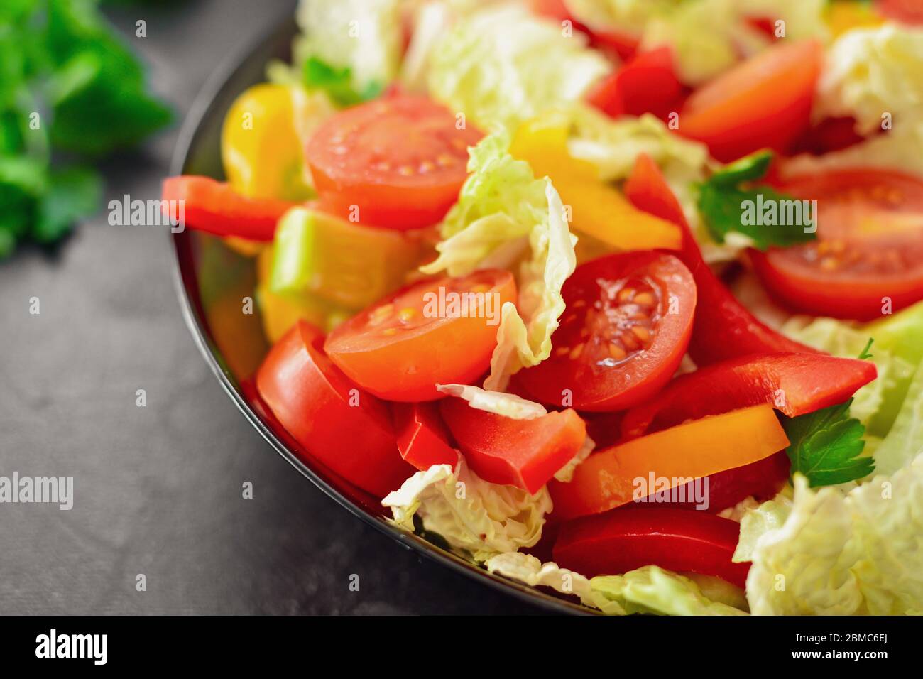 Spring vegetable salad. Salad, tomatoes, cabbage, dressing, bell pepper, cucumber, parsley. Dark background, top view. Close up. Stock Photo