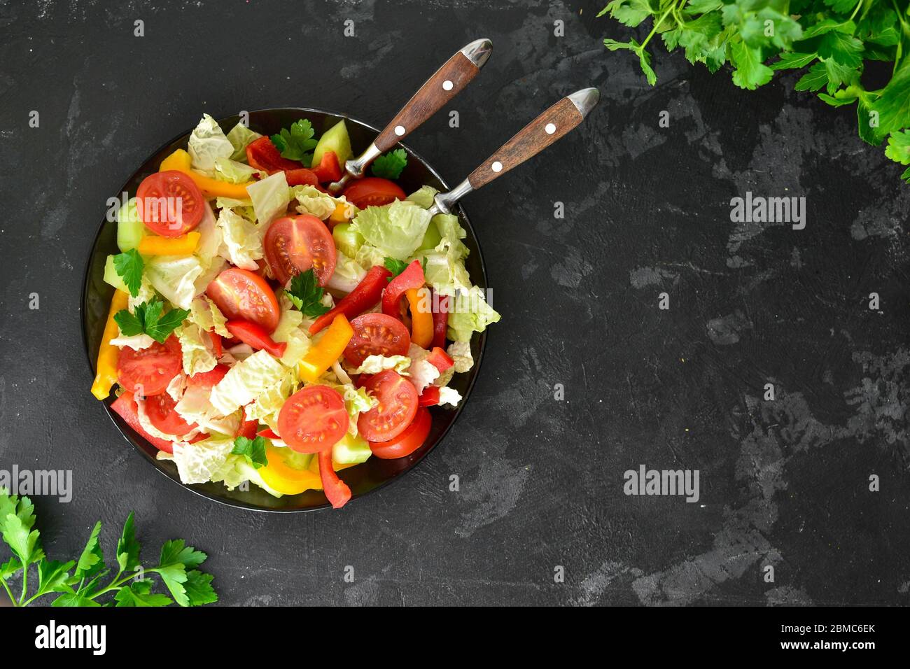 Spring vegetable salad. Salad, tomatoes, cabbage, dressing, bell pepper, cucumber, parsley. Dark background, top view. Healthy vegetarian and vegan Stock Photo
