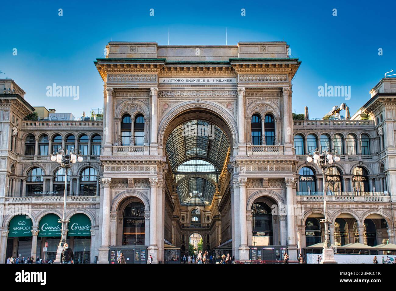 Milan, Italy May 8, 2020: The golden sunshine is reflecting on the front of the magnificent triumphal arch entrance of the Galleria Vittorio Emanuele Stock Photo