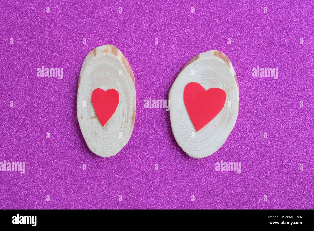 Two red hearts lie on a cut tree on a pink background. Valentine's day, Mother's Day, on March 8, minimal concept. Greeting card with a heart on a pin Stock Photo