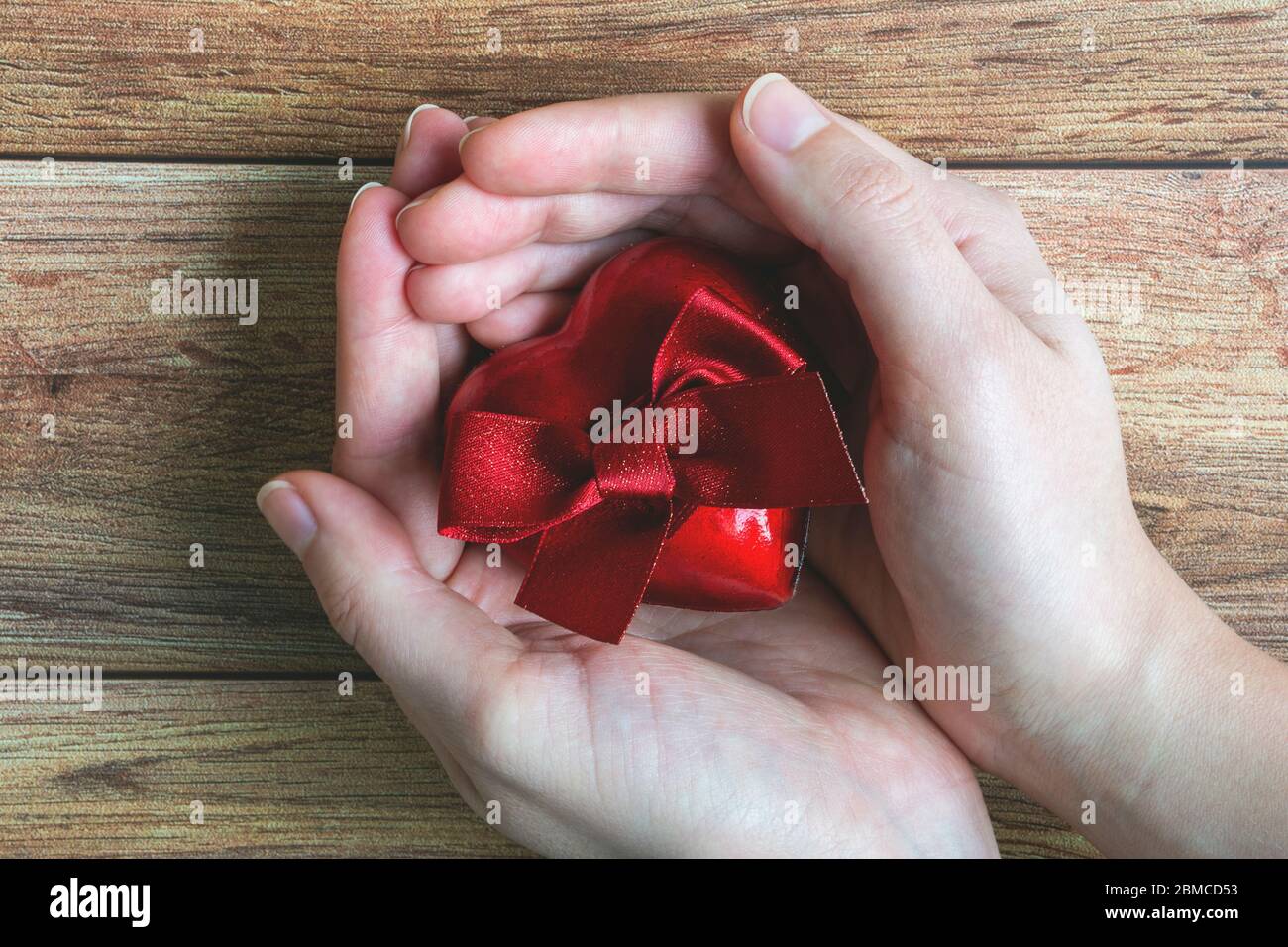 Woman hands holding a red gift heart with bow on wooden background. Valentine's day, mother's day, birthday, celebration, giving Stock Photo