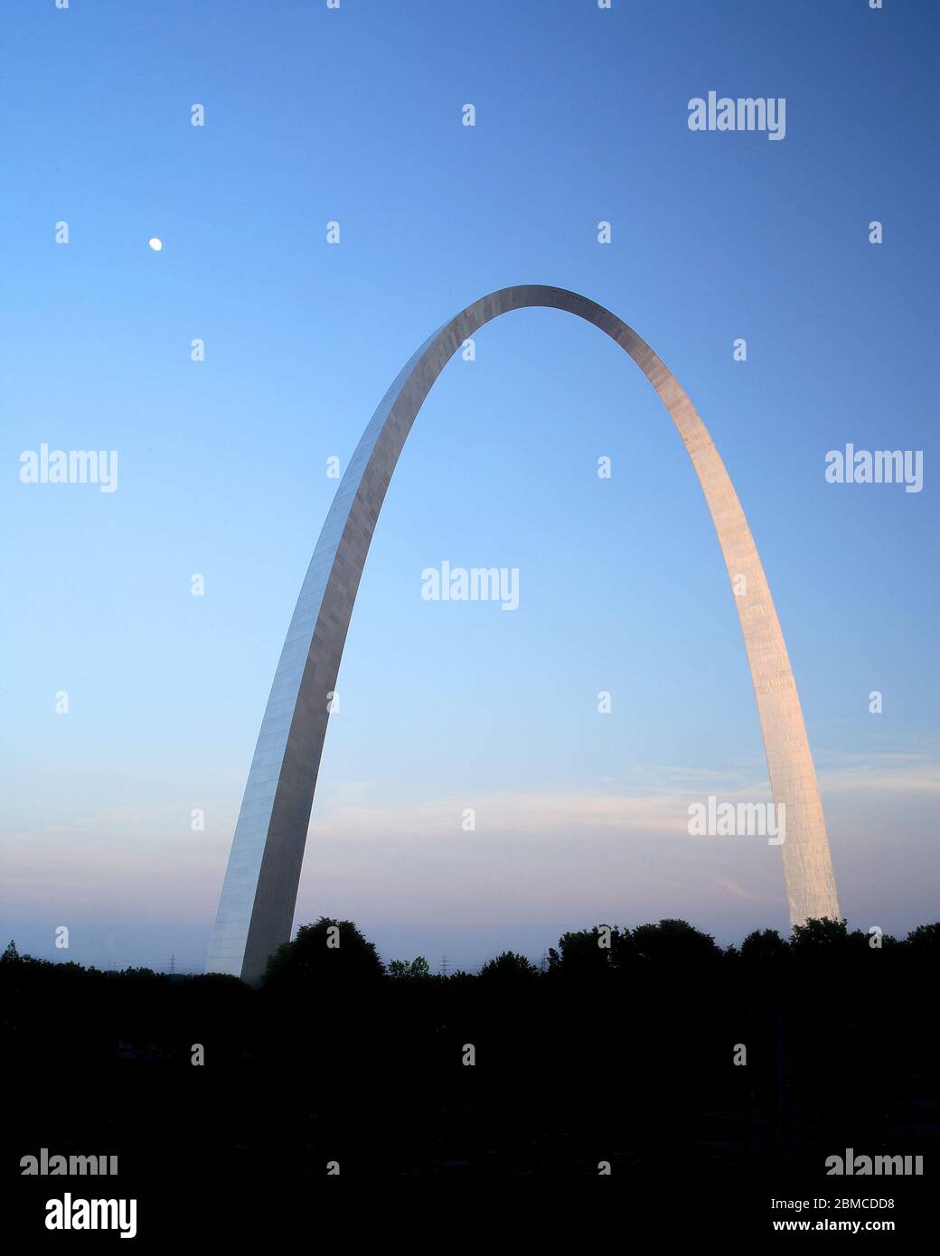 The Gateway Arch in St. Louis at sunset shows the moon rising in the dusk as the last light of the day reflects off the stainless steel monument. Stock Photo