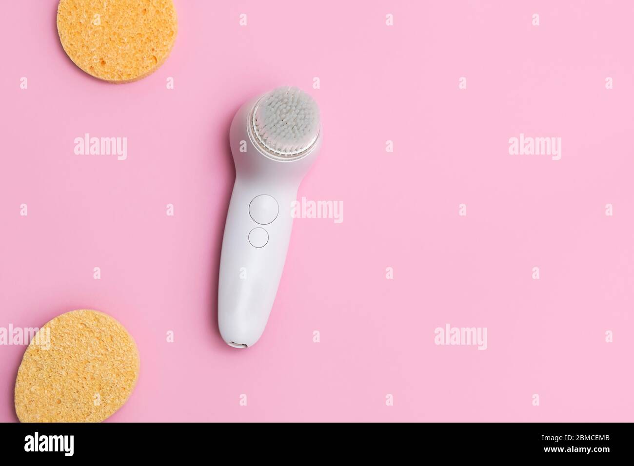 Top view of electric facial brush and face sponges on soft pink background with space for text Stock Photo