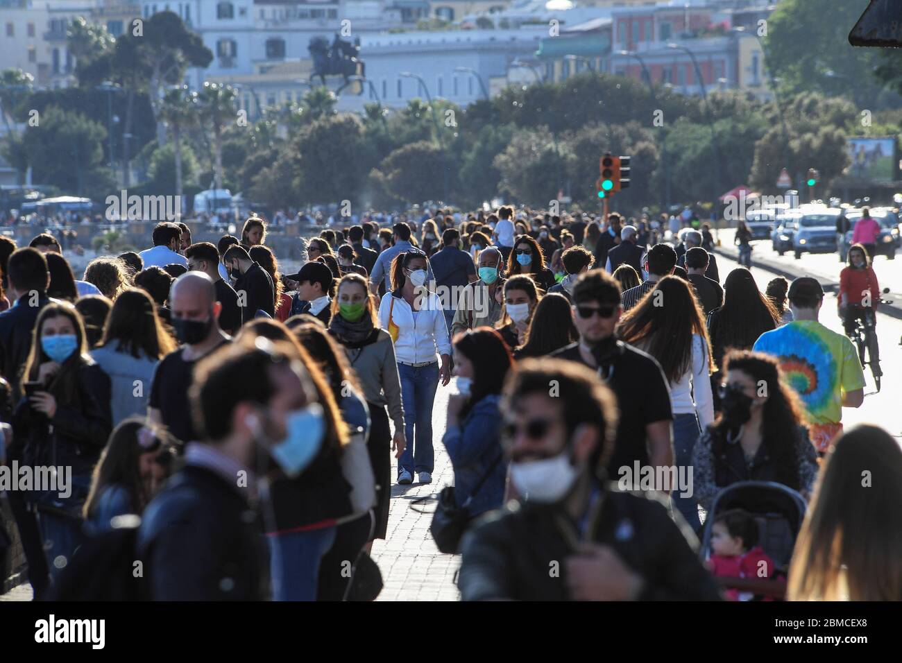 People in protective masks stroll along the Caracciolo seafront in Naples, southern Italy. The Italian government announced a gradual lifting of the lockdown restrictions that were implemented to stem the widespread of the SARS-CoV-2 coronavirus that causes the COVID-19 disease. Stock Photo