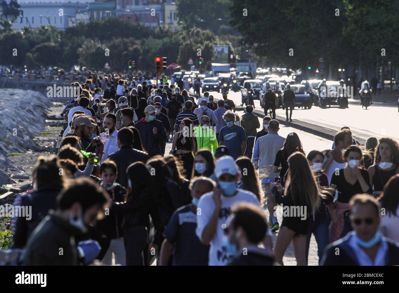 People in protective masks stroll along the Caracciolo seafront in Naples, southern Italy. The Italian government announced a gradual lifting of the lockdown restrictions that were implemented to stem the widespread of the SARS-CoV-2 coronavirus that causes the COVID-19 disease. Stock Photo