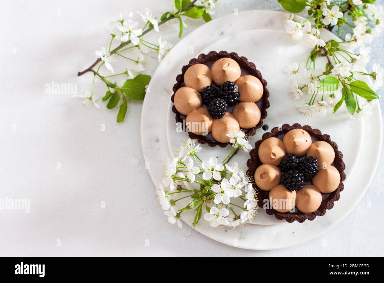 Chocolate tart with salted caramel filling and fresh blackberries. Cherry flowers on background. Copy space. Stock Photo