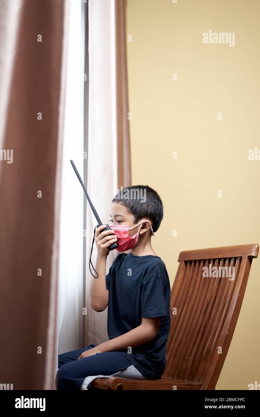 Sad little Boy communicate using walkie talkie and looking through window at home quarantine Stock Photo