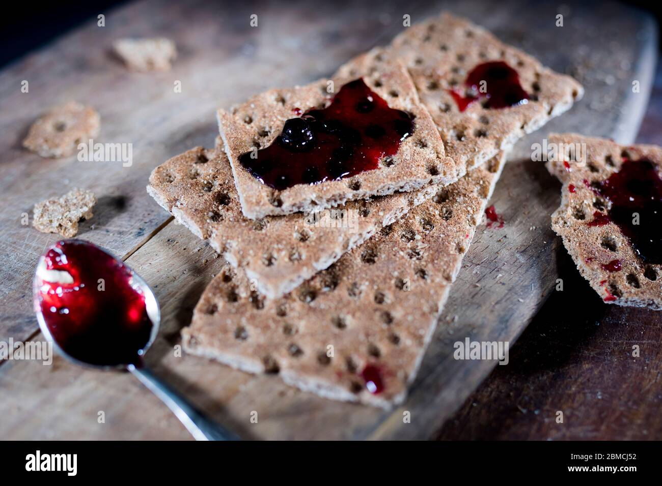 Open jar with blackcurrant jam on a wooden cutting board. Dry biscuits spread with jam, crumbs and a spoon in jam. Space for text. Stock Photo