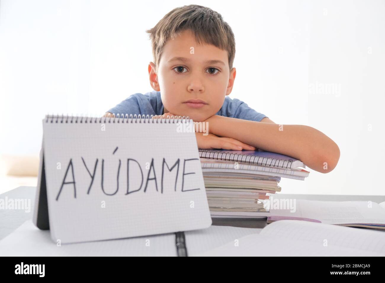Tired frustrated boy sitting at the table with many books. Spanish word