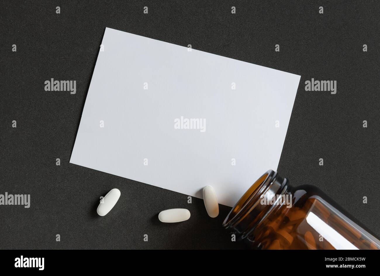 White tablets pills spilling out of a toppled brown bottle over dark background Stock Photo