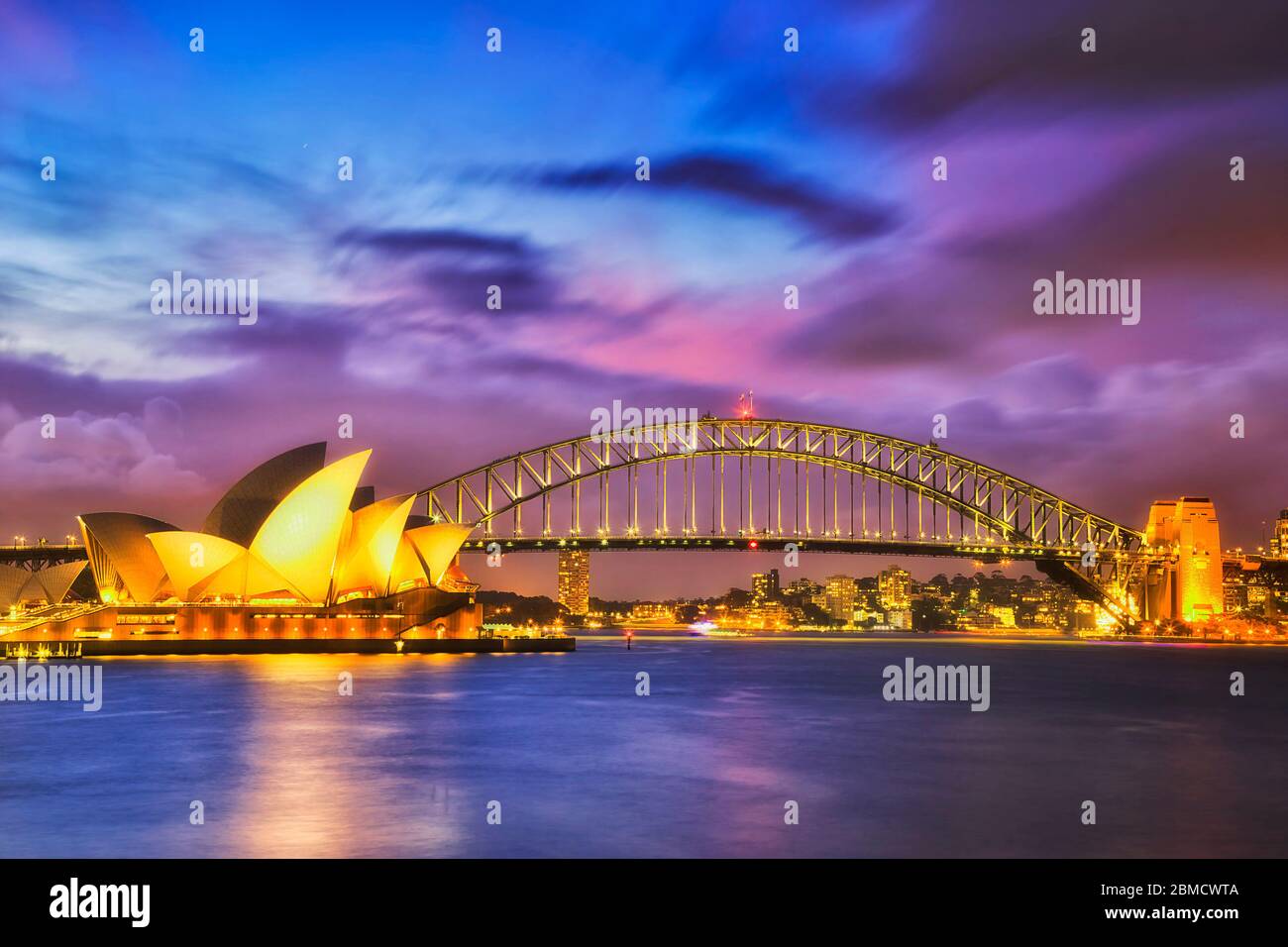 Waterfront of Sydney city CBD on shores of Sydney Harbour around the harbour bridge at sunset with blurred water and clouds. Stock Photo